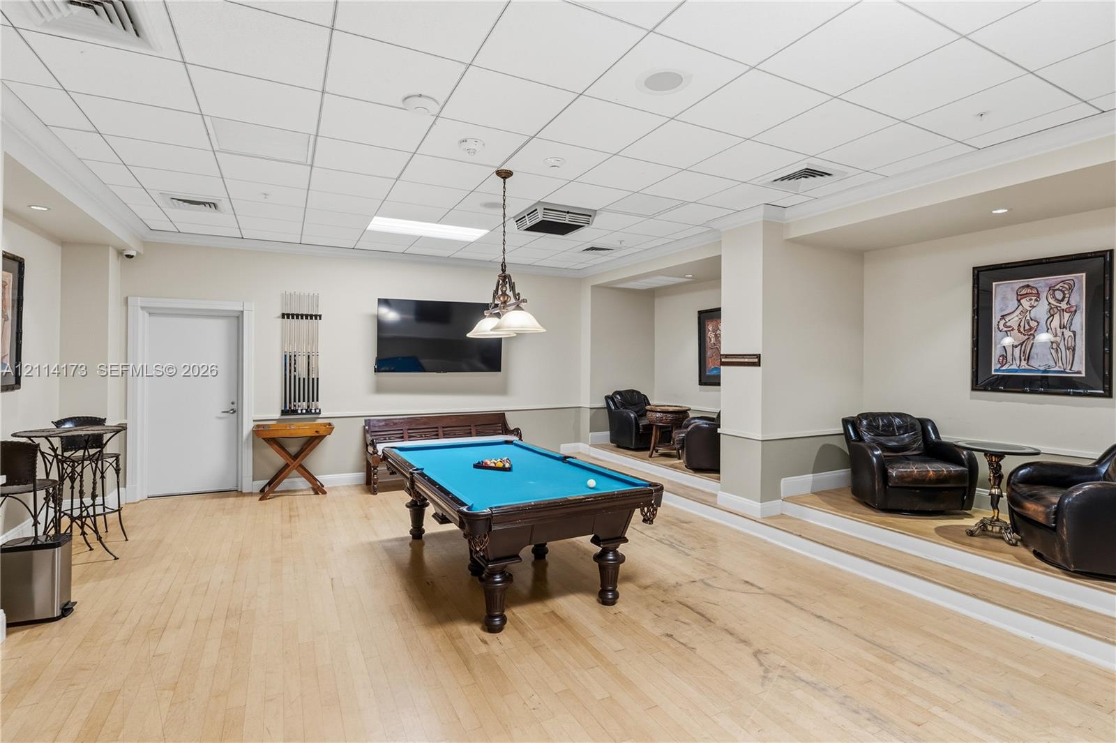 Multi-purpose space featuring wood-finish flooring, a raised platform seating area, a suspended multi-light fixture, and recessed lighting