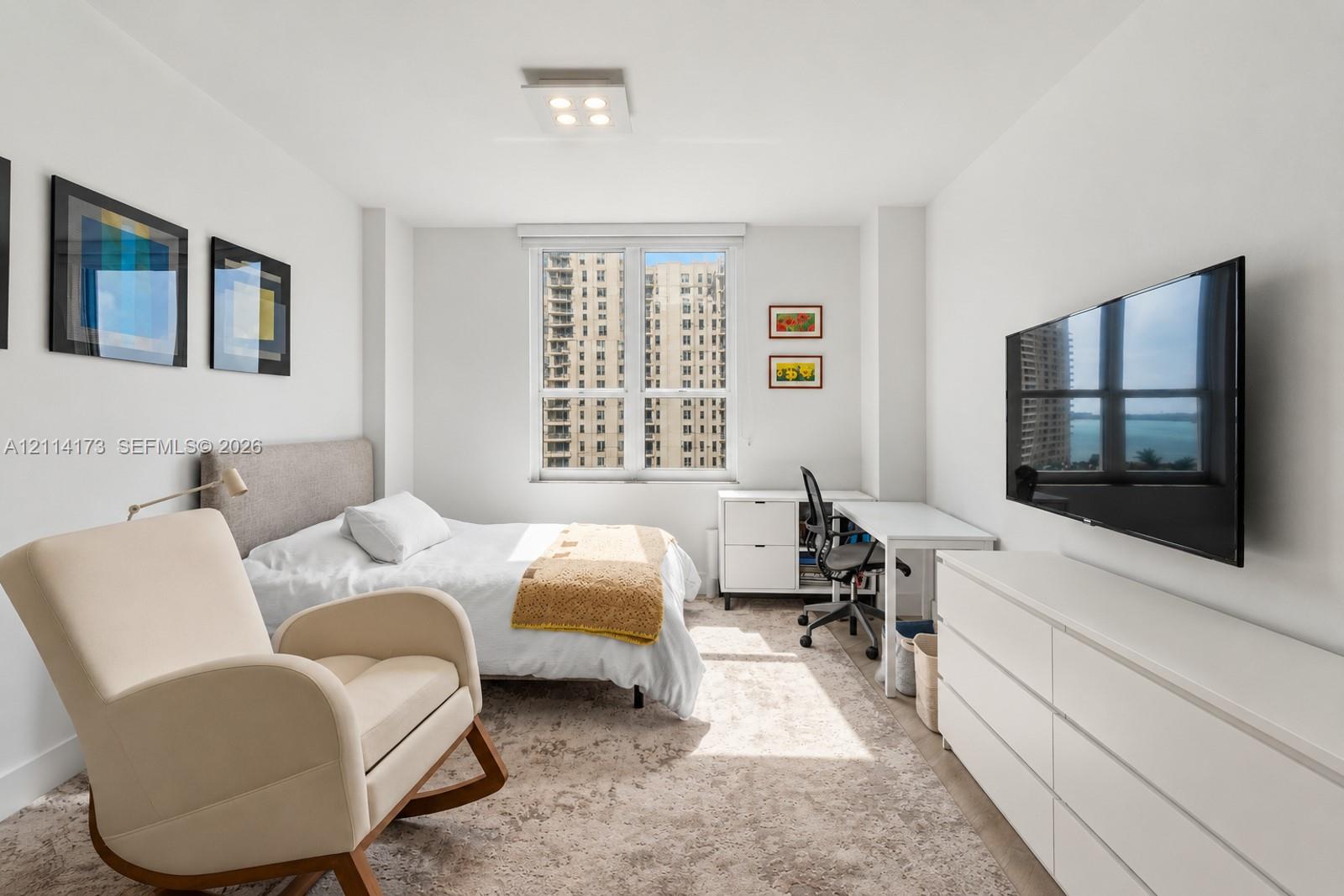 Bright interior space featuring a large window with urban and water scenery, neutral wall finishes, and a modern ceiling-mounted light fixture