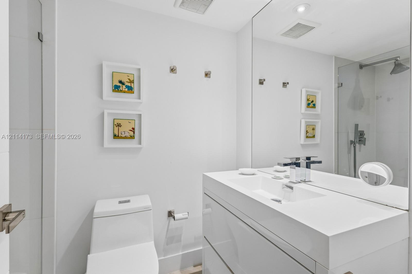 Modern floating vanity with a seamless integrated sink, polished chrome widespread faucet, large-format mirror, and glass-enclosed shower featuring a wall-mounted rainfall showerhead