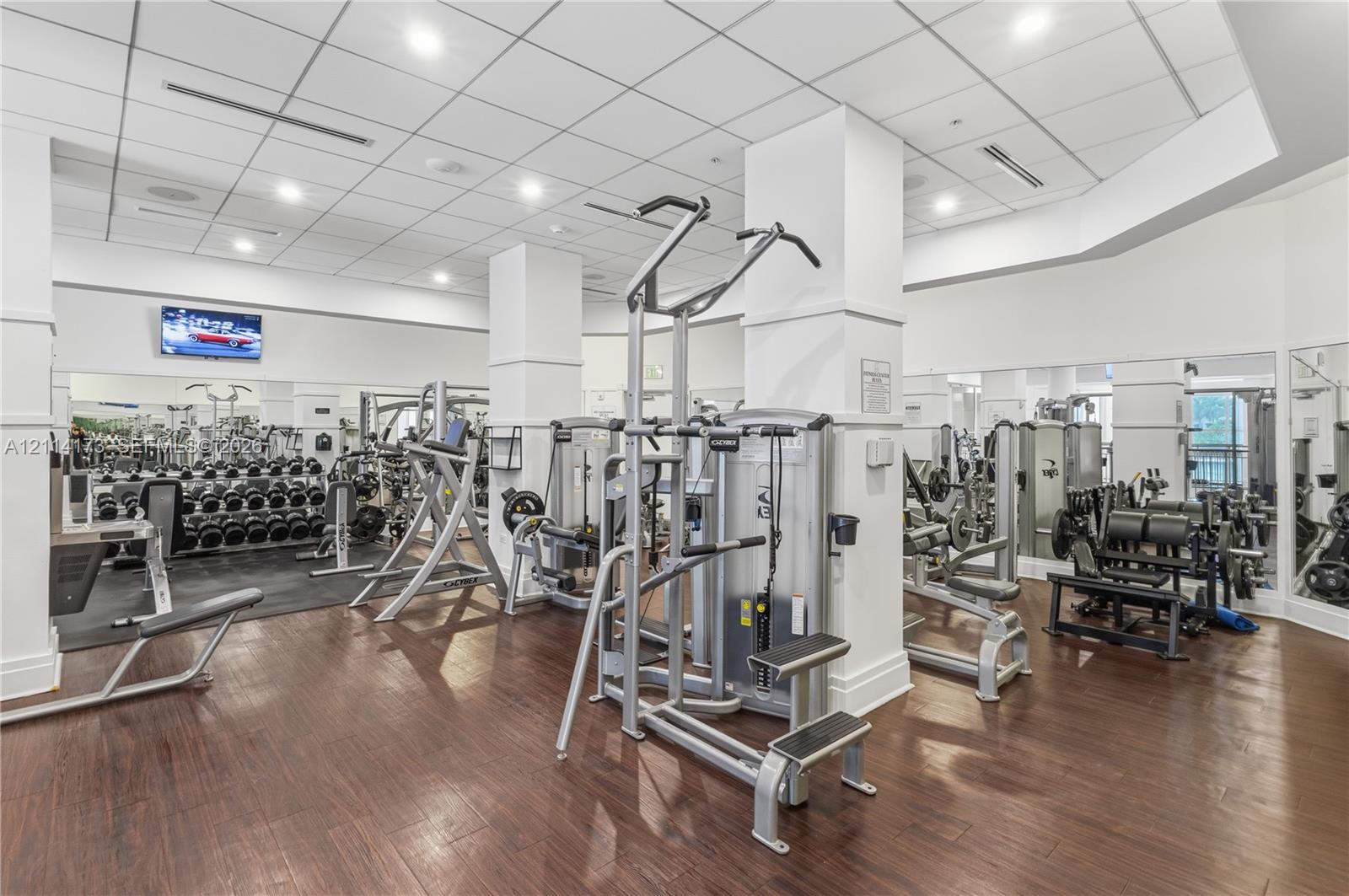 Fitness center featuring wood-finish flooring, recessed lighting, drop ceiling panels, and full-length wall mirrors