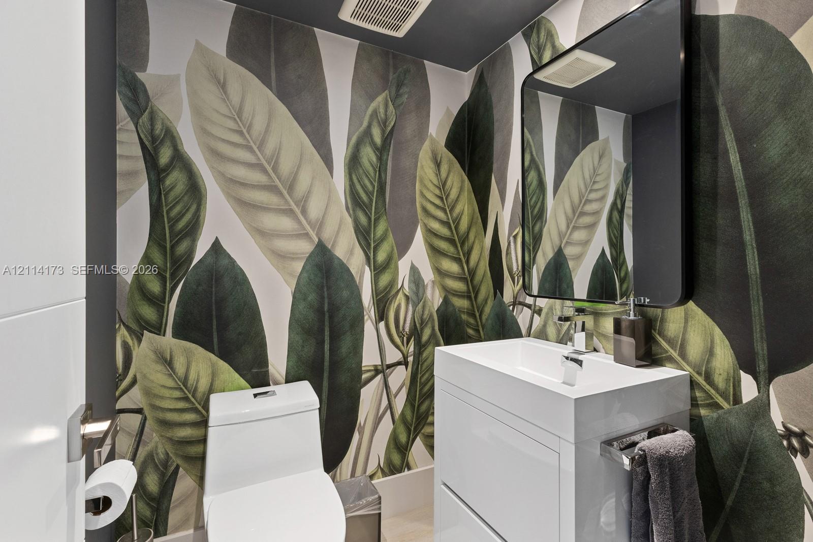 Botanical print wallcovering, white vanity cabinet with a rectangular basin, polished chrome faucet, and black-framed rectangular wall mirror