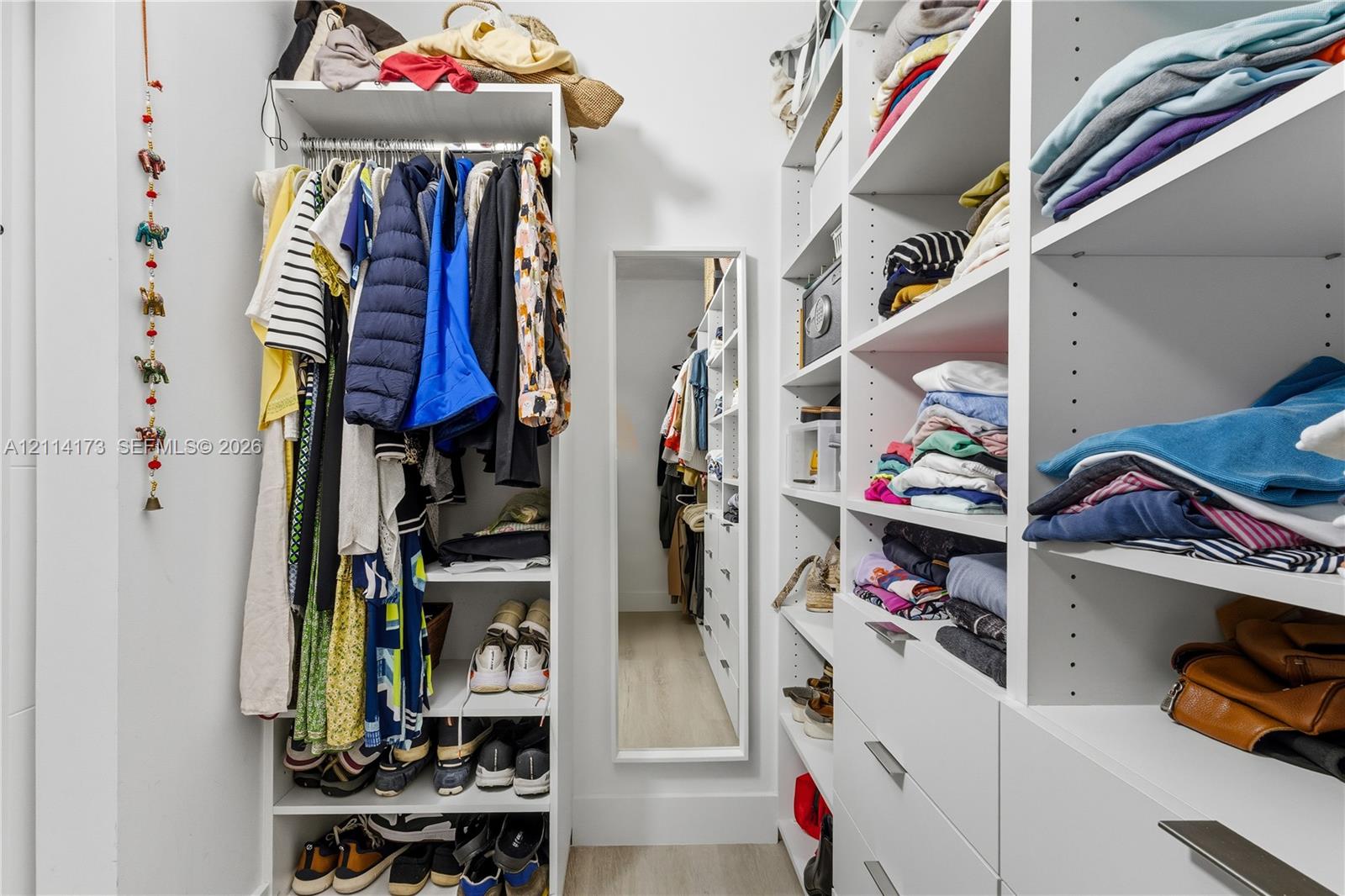 Walk-in closet featuring extensive built-in white shelving, integrated clothing rods, multiple pull-out drawers with metal hardware, and a full-length wall-mounted mirror