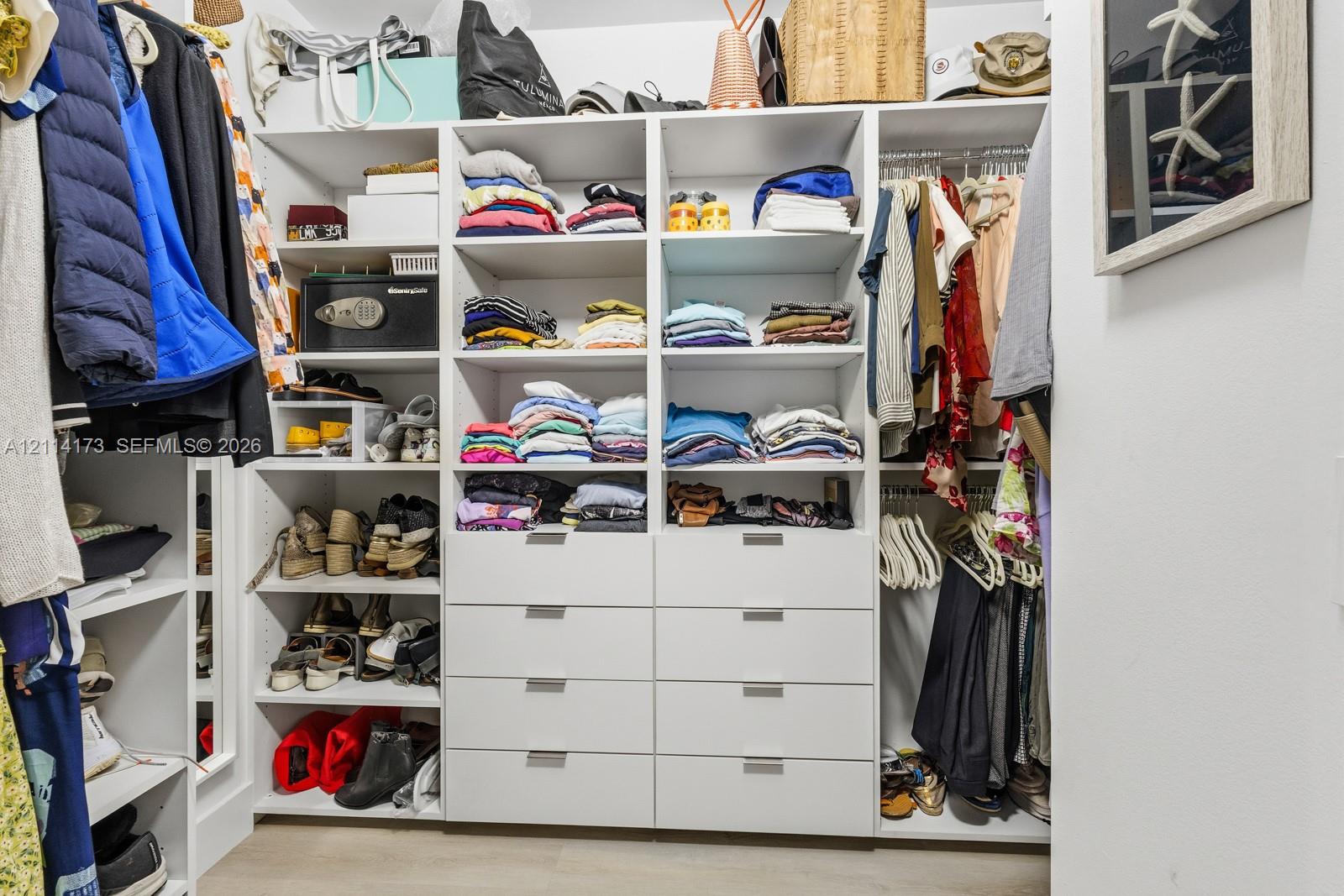Custom walk-in closet featuring floor-to-ceiling white shelving, integrated hanging rods, eight pull-out storage drawers, and sleek metal hardware