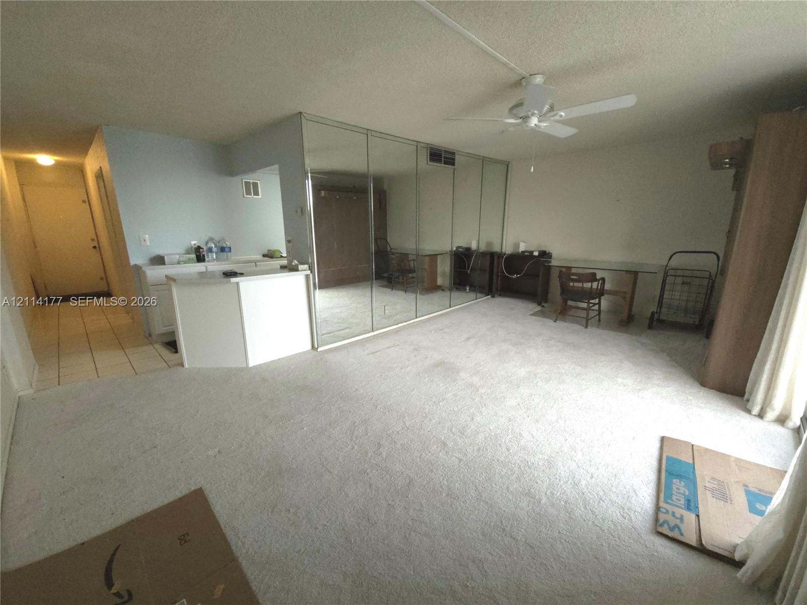 Spacious interior featuring full-wall mirrored closet doors, white built-in cabinetry, ceiling fan, and tile flooring in the entry area