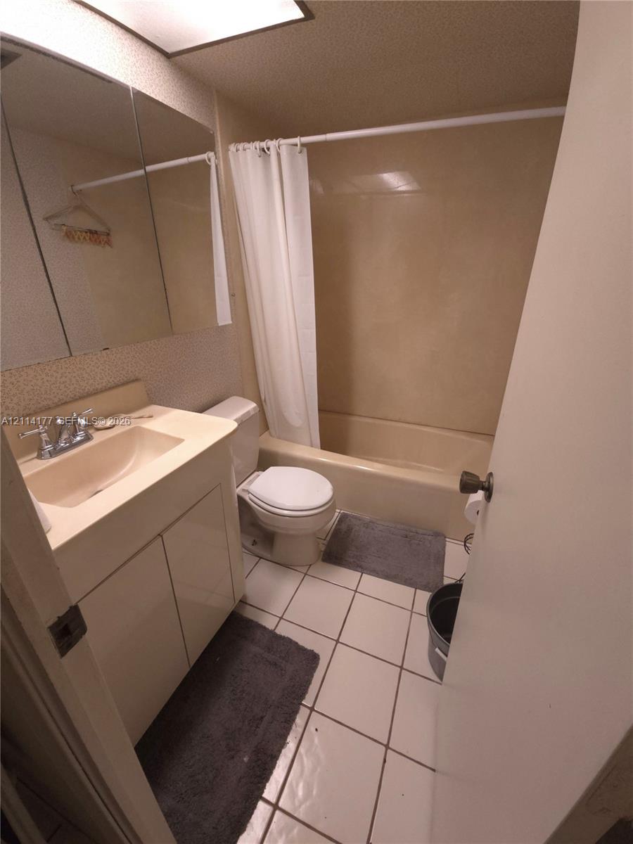 Bathroom featuring a single-sink vanity with integrated basin, medicine cabinet, tiled flooring, and a combined tub and shower enclosure