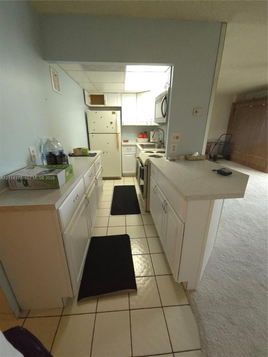 Kitchen featuring white cabinetry, solid-surface countertops, tile flooring, and integrated white appliances