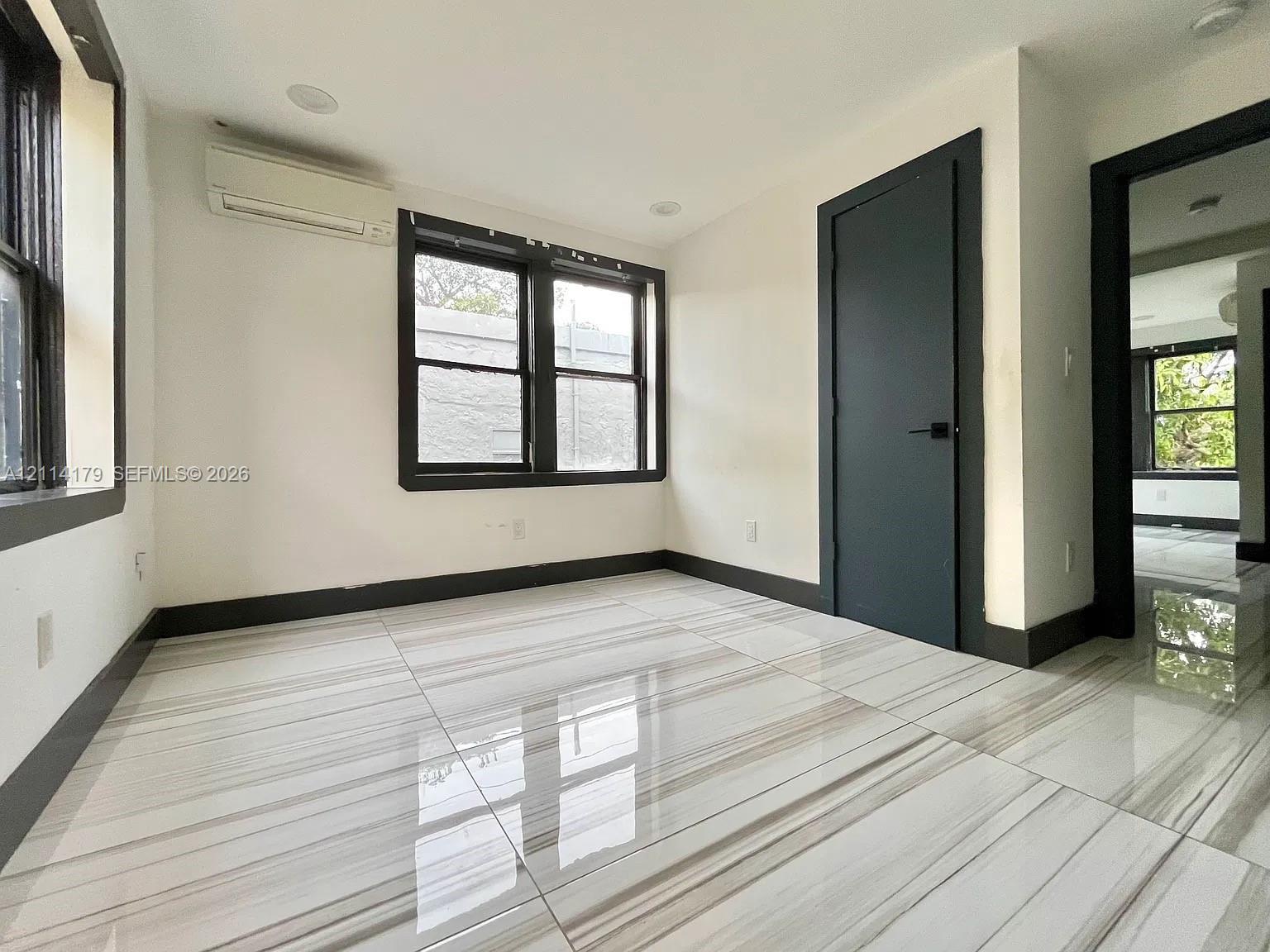 Large-format stone-look tile flooring with high-contrast veining, dark-framed dual-pane windows, recessed ceiling lighting, and a wall-mounted ductless climate control unit