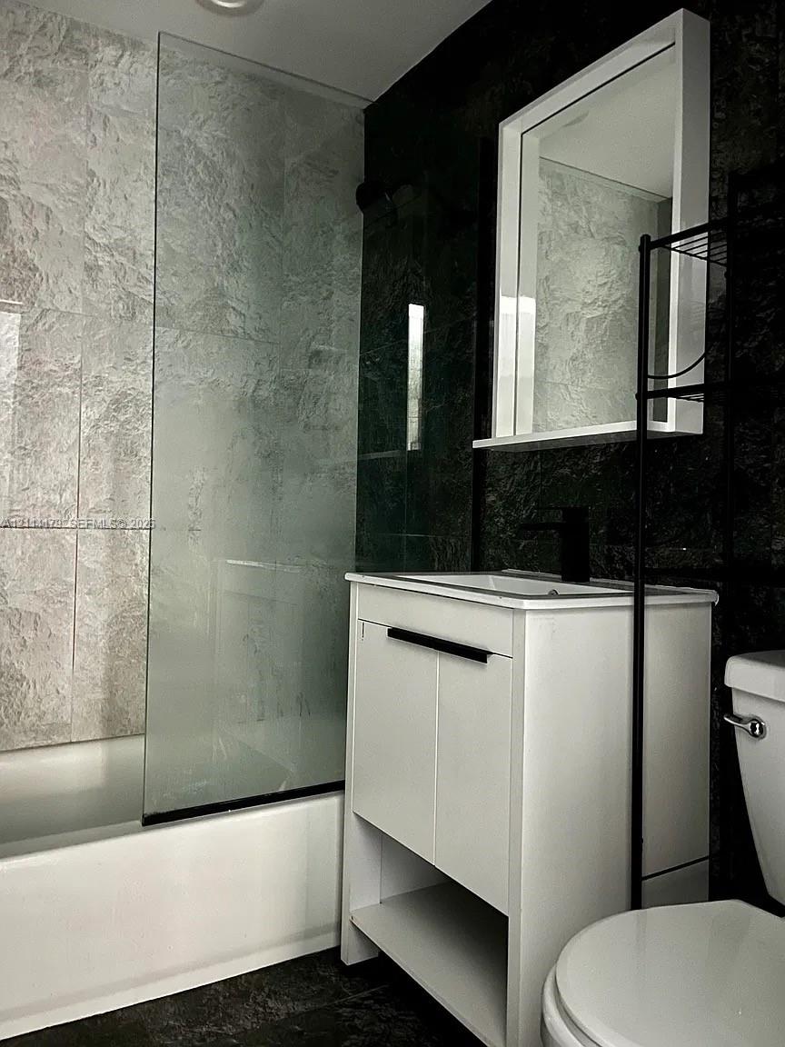 White vanity featuring integrated shelving and a dark-finish faucet, paired with a glass shower screen and dual-tone wall tile detailing