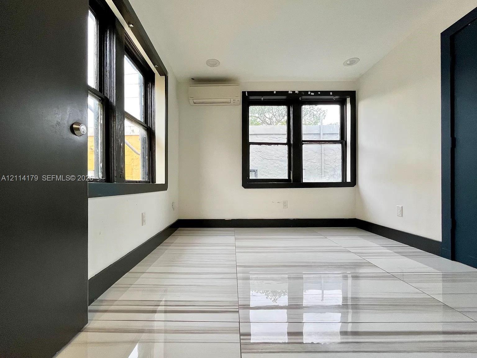 Interior room featuring polished tile flooring with linear veining, dark-trimmed windows, recessed ceiling lighting, and a wall-mounted ductless climate control unit