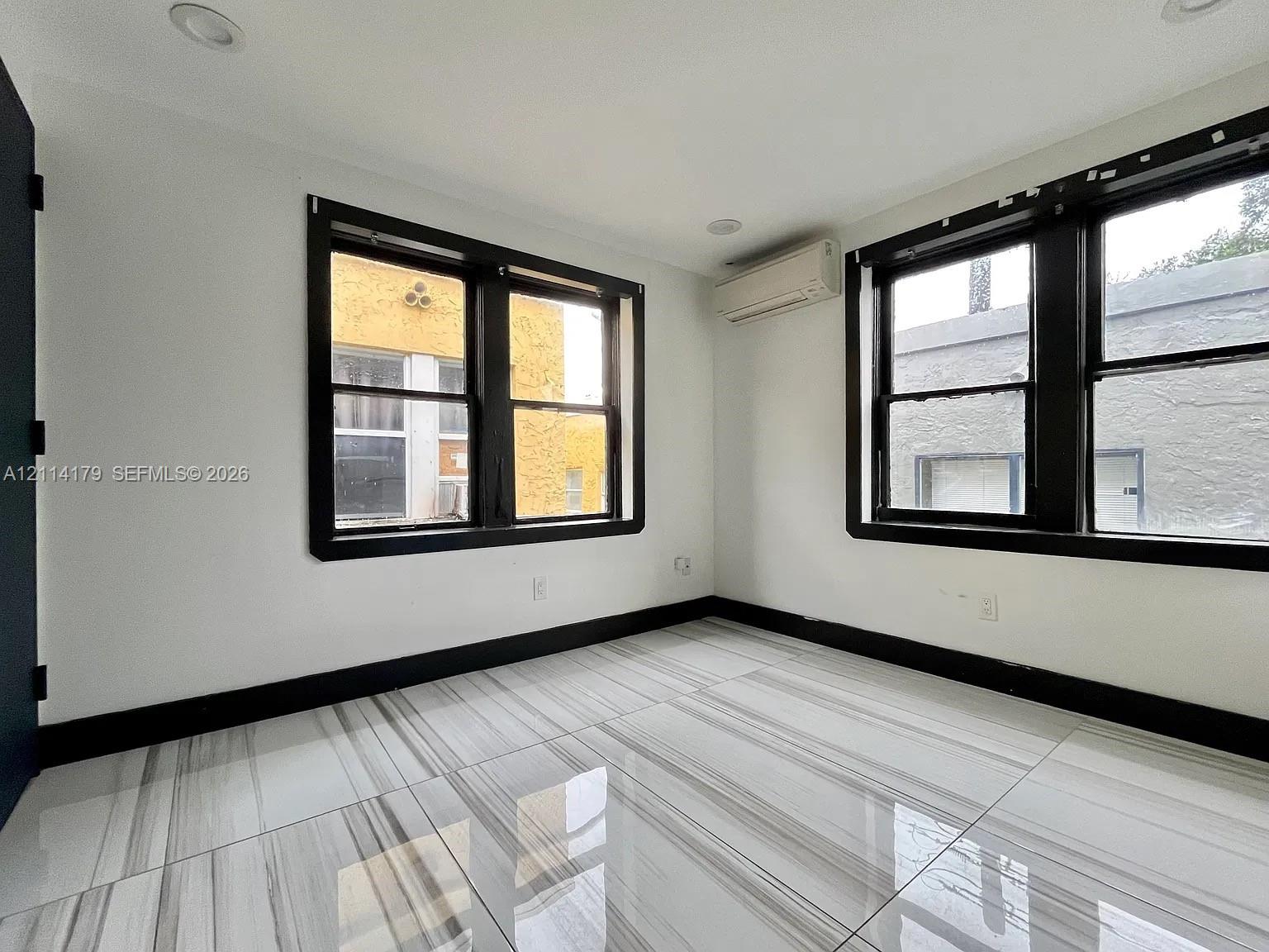 Room featuring large-format porcelain tile flooring, high-contrast black window frames, recessed ceiling lighting, and a wall-mounted ductless heating and cooling unit