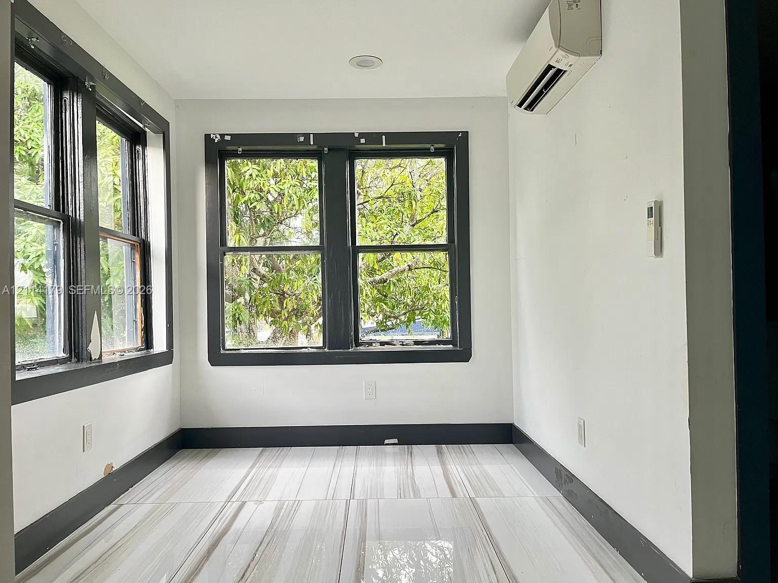 Neutral-toned stone-finish tile flooring, contrasting dark-framed windows, and a wall-mounted ductless climate control unit