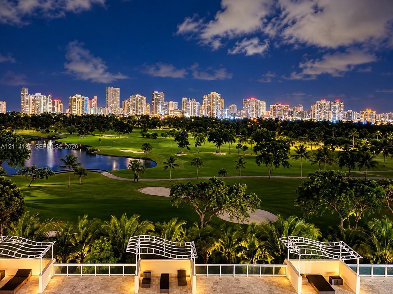 Outdoor terrace featuring natural stone flooring, decorative white metal pergolas, and white glass panel railings, overlooking a golf course with water features and a distant cityscape