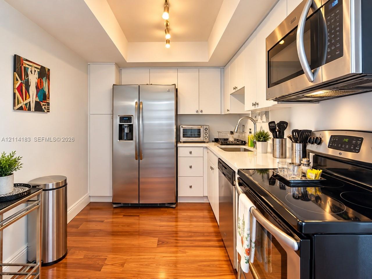 Kitchen featuring white cabinetry, solid-surface countertops, stainless steel appliances, recessed ceiling lighting, and wood-finish flooring