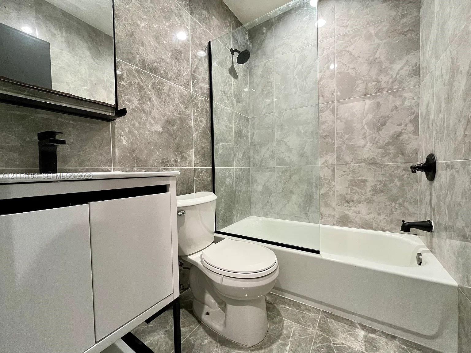 Bathroom featuring floor-to-ceiling stone-patterned wall tile, white vanity with black hardware, glass shower enclosure, and matte black plumbing fixtures