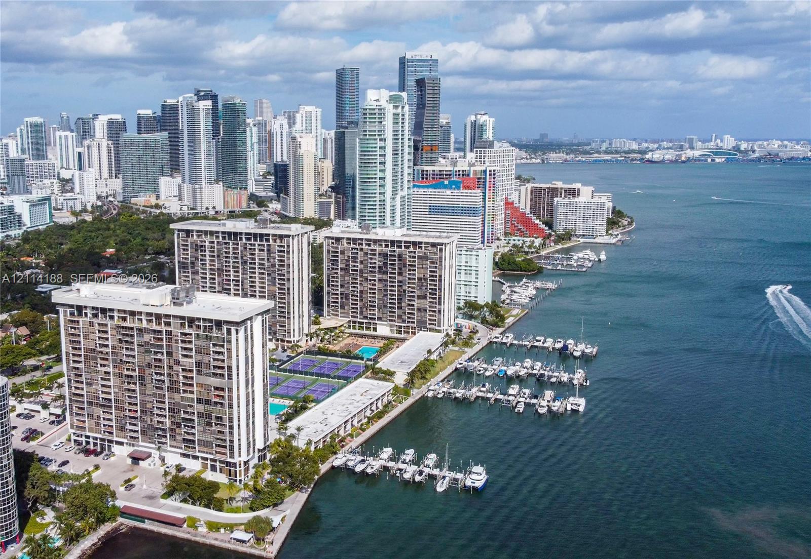 High-rise residential complex featuring multiple tennis courts, a swimming pool, and private deep-water boat slips along the waterfront