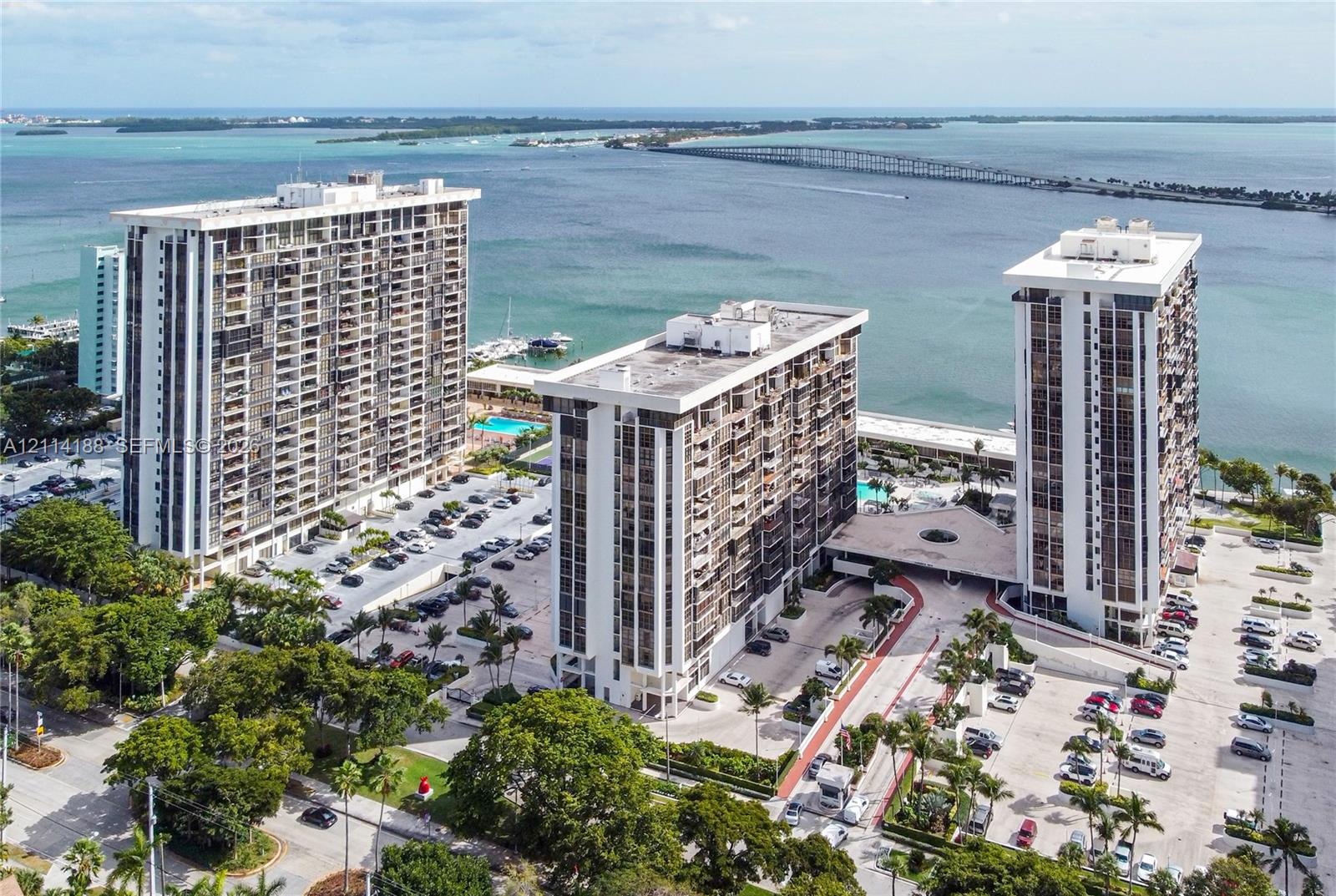 High-rise coastal residential complex featuring structured surface parking, paved driveways, swimming pool access, and mature landscaping
