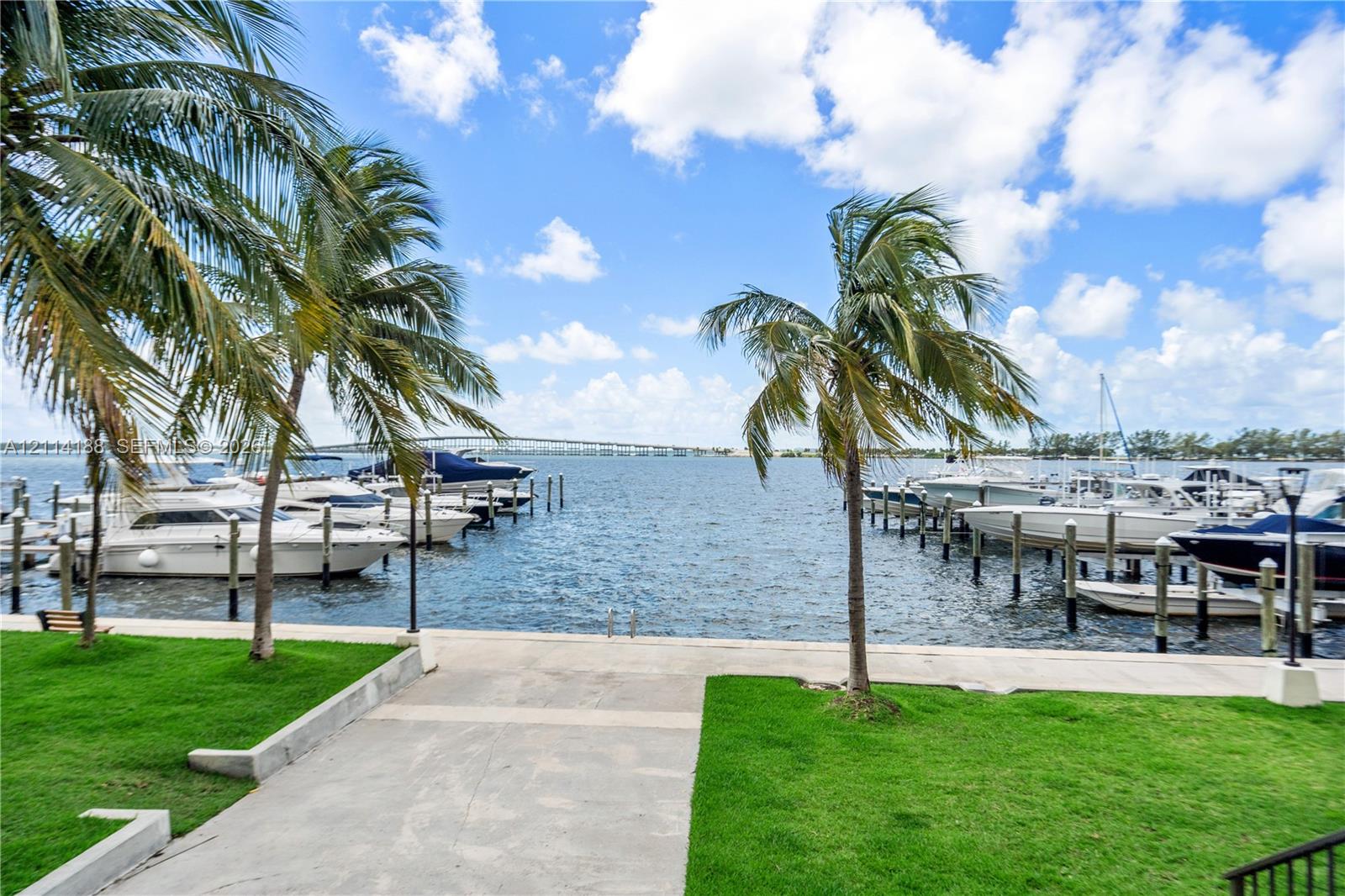 Waterfront property grounds featuring a concrete bulkhead, private boat slips, manicured lawn, and mature palm trees