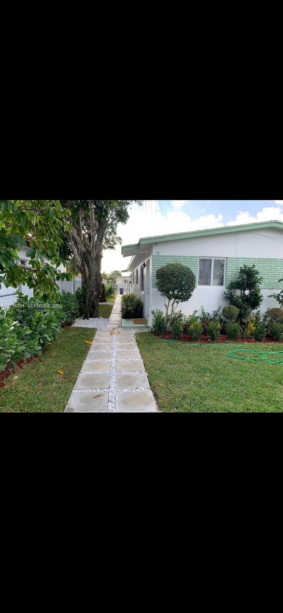 Exterior side grounds featuring a concrete paver walkway, manicured lawn, established shrubbery, and mature trees