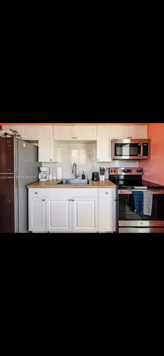 Kitchen featuring white shaker-style cabinetry, wood-finish countertops, stainless steel appliances, and a tile backsplash