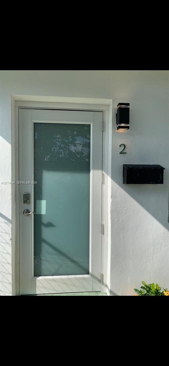 Entry door featuring a white frame, large vertical frosted glass panel, electronic deadbolt, exterior wall-mounted black lantern-style sconce, and attached black mailbox