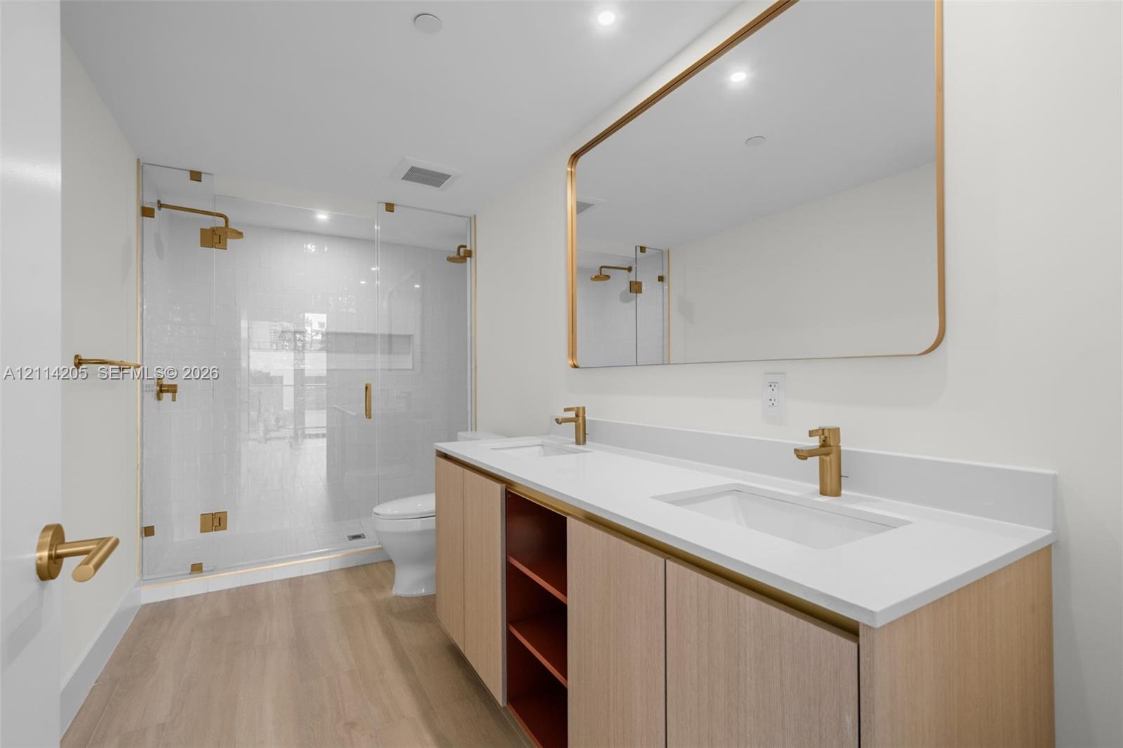 Master bathroom Dual-sink vanity with light wood cabinetry, white countertop, and gold-finish fixtures, complemented by a glass-enclosed walk-in shower with gold-finish hardware and wood-finish flooring Master bathroom Dual-sink vanity with light wood cabinetry, white countertop, and gold-finish fixtures, complemented by a glass-enclosed walk-in shower with gold-finish hardware and wood-finish flooring