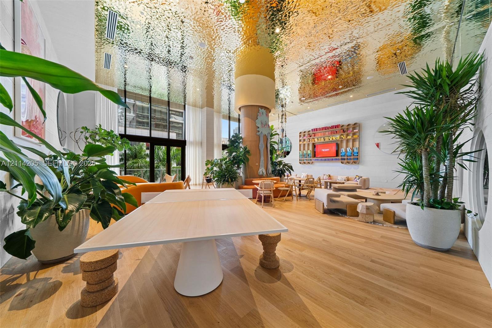 Common area featuring a reflective, textured metallic ceiling, wood-finish flooring, floor-to-ceiling glass windows, and a central structural column