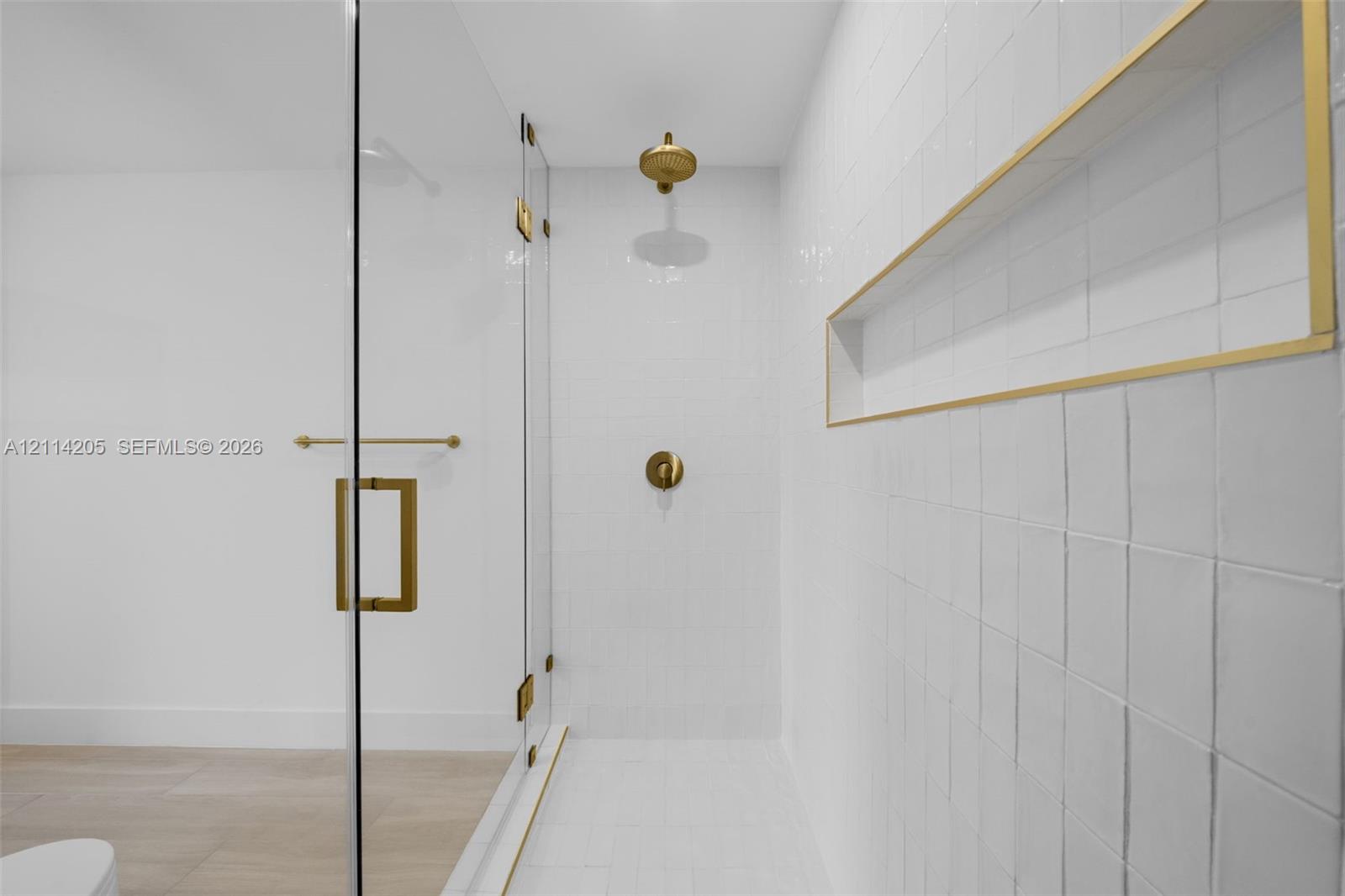 Walk-in shower featuring a frameless glass enclosure, gold-toned hardware, white wall tile, integrated recessed shelving, and a rain-style showerhead