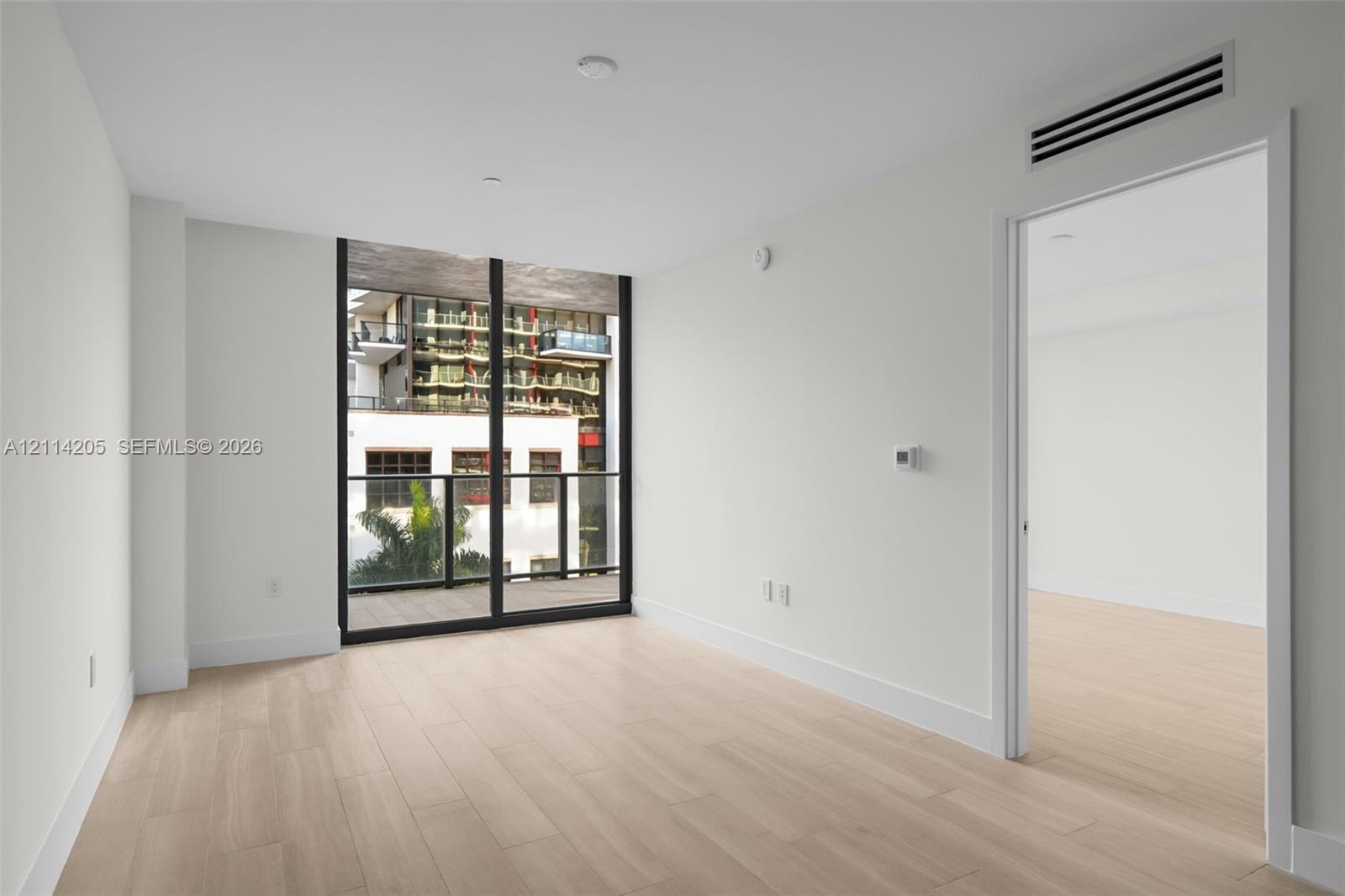 Floor-to-ceiling windows, wood-finish flooring, and an attached balcony with dark metal railings