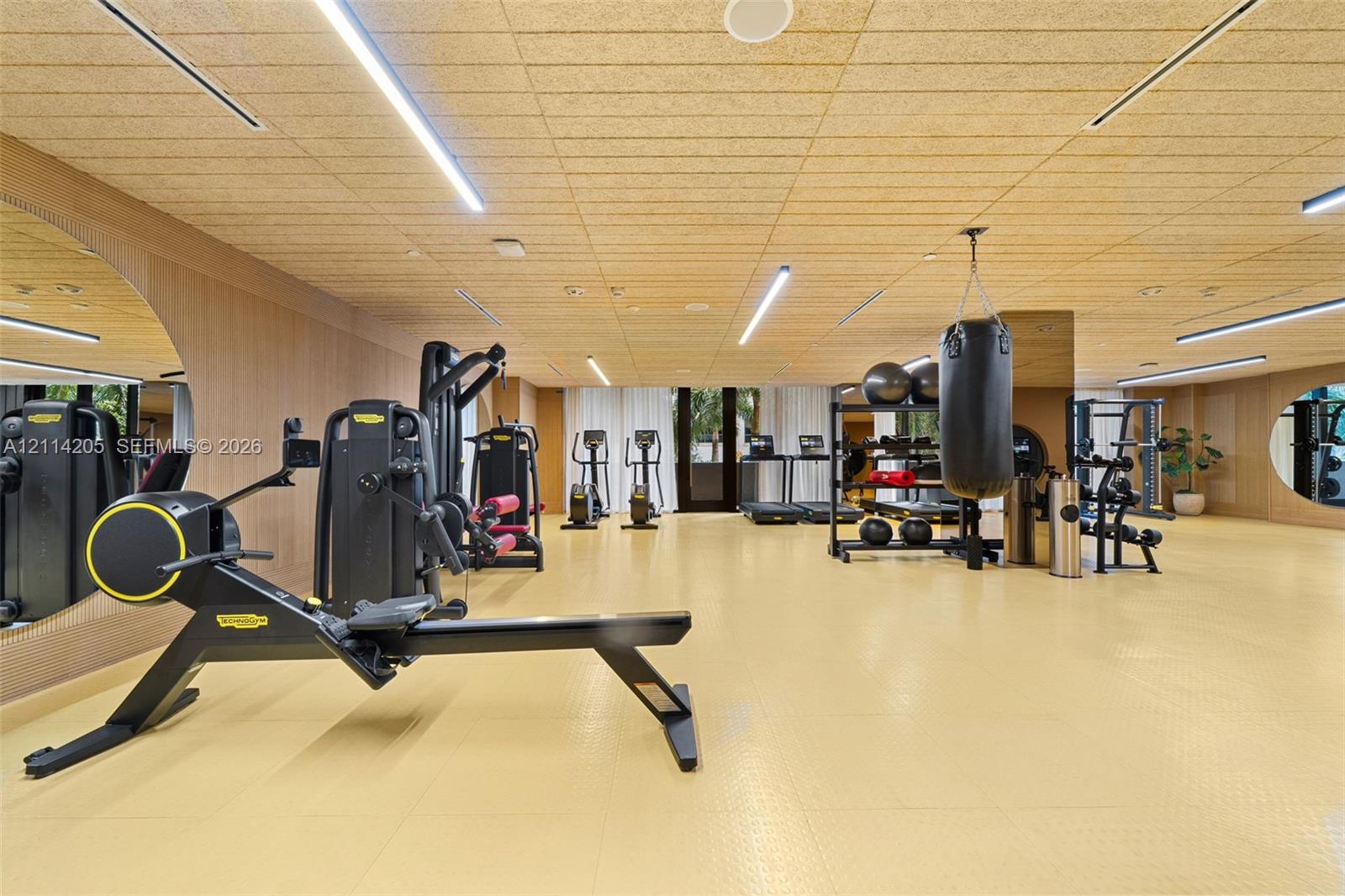 Fitness space featuring wood-panel wall cladding, textured acoustic ceiling panels, wall-to-wall integrated mirrors, and recessed linear lighting