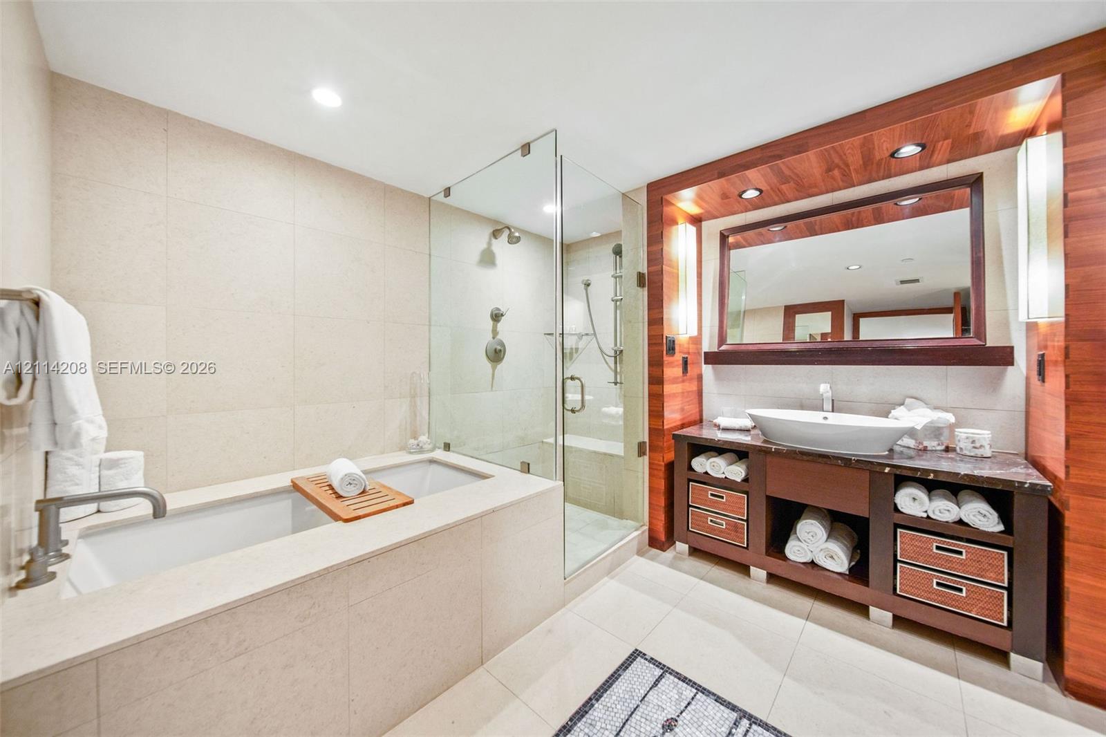 Bathroom featuring a built-in stone-surround tub, glass-enclosed shower with handheld fixture, wood-paneled vanity with integrated vessel sink, and recessed lighting