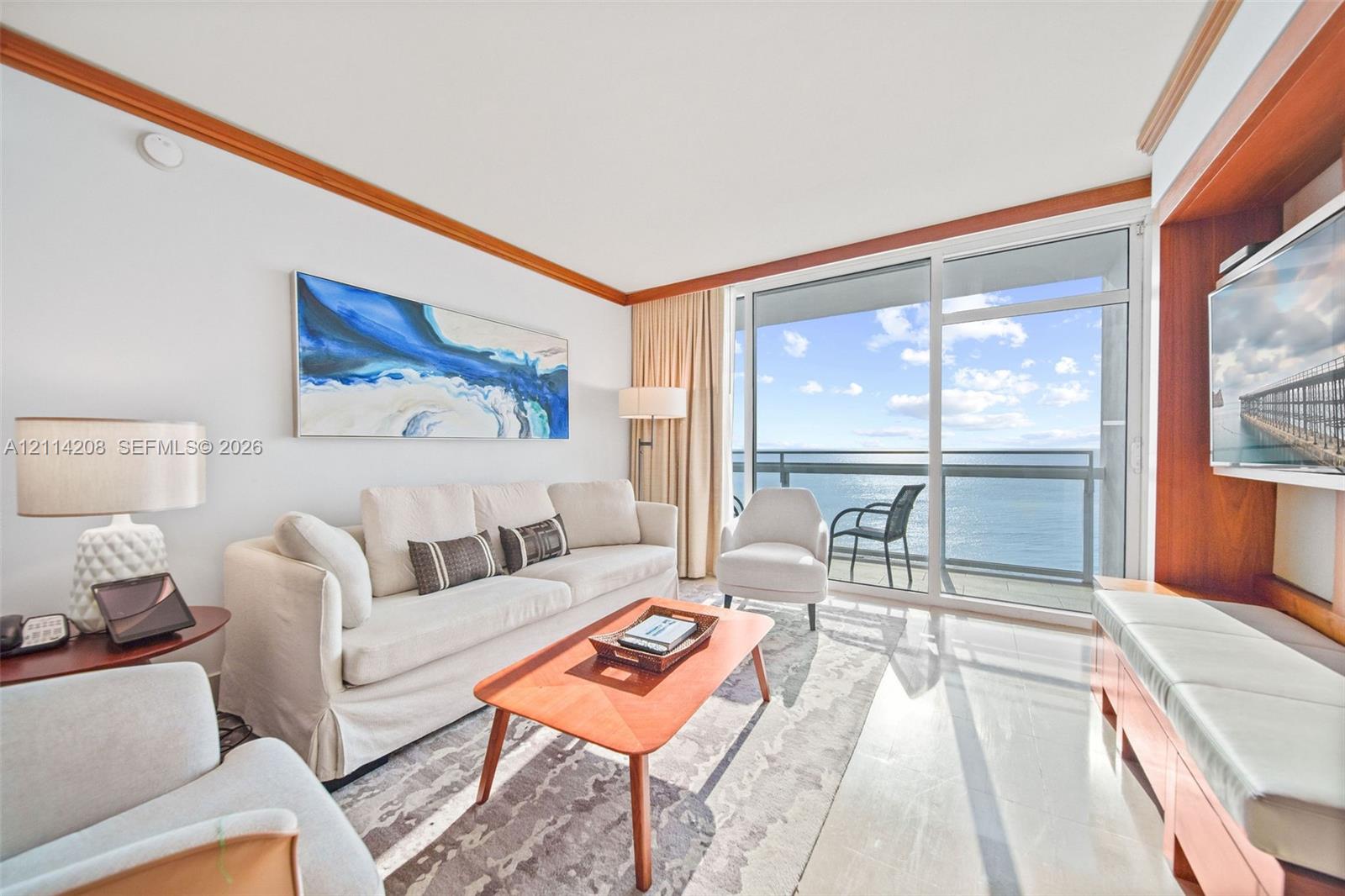 Floor-to-ceiling glass sliding doors opening to an exterior balcony, built-in wooden media cabinetry, polished stone flooring, and crown molding