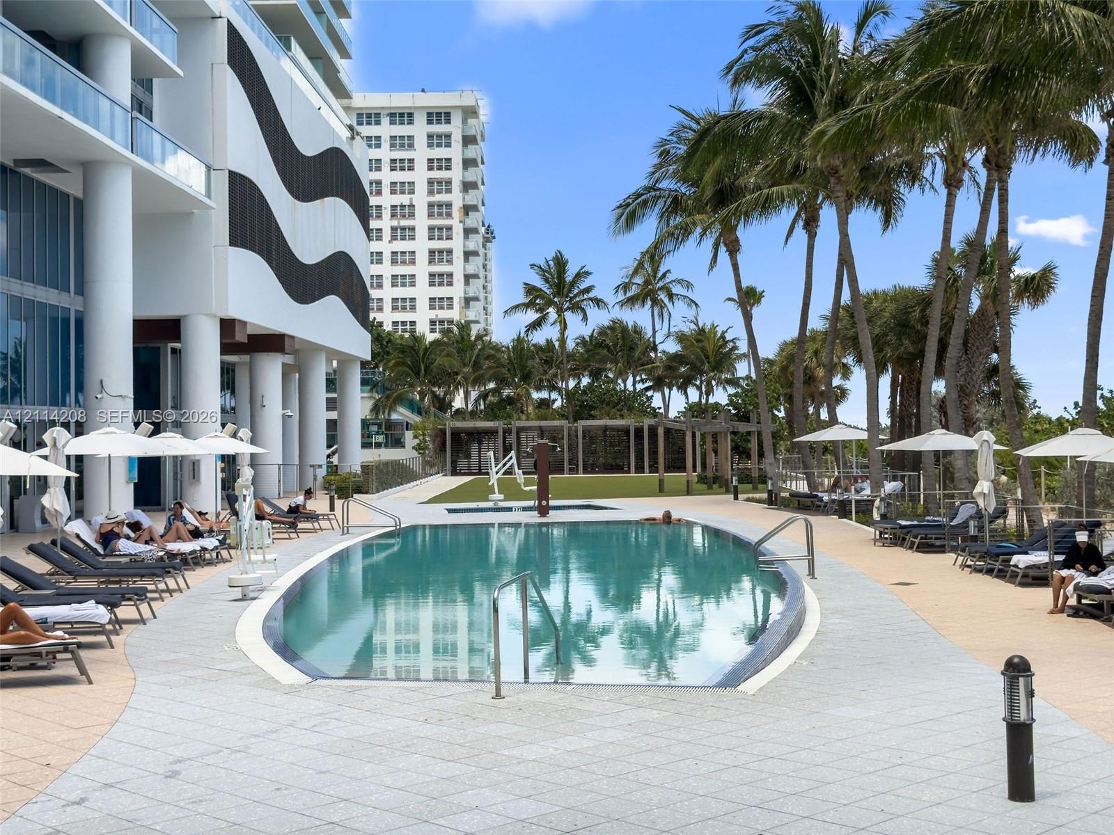 Outdoor swimming pool featuring a curved concrete deck, metallic handrails, and surrounding mature palm trees