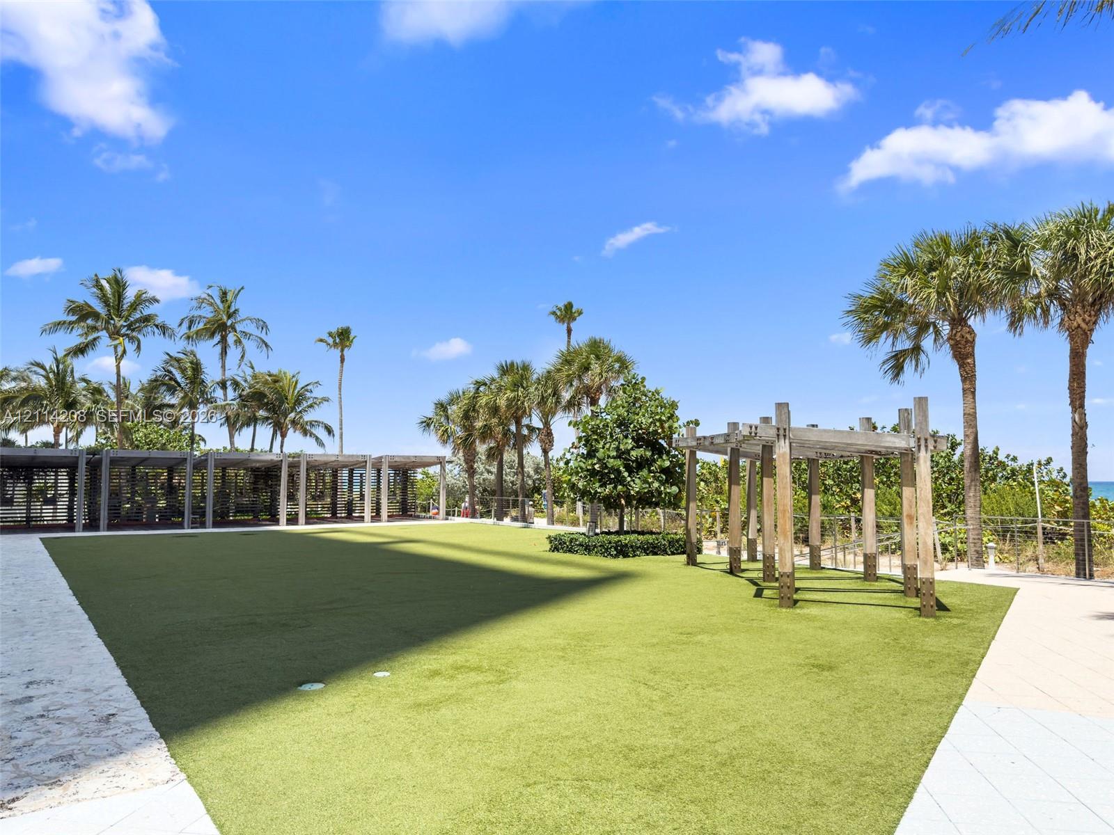 Outdoor recreation area featuring artificial turf, wooden pergola structures, and paved walkways surrounded by mature palm trees
