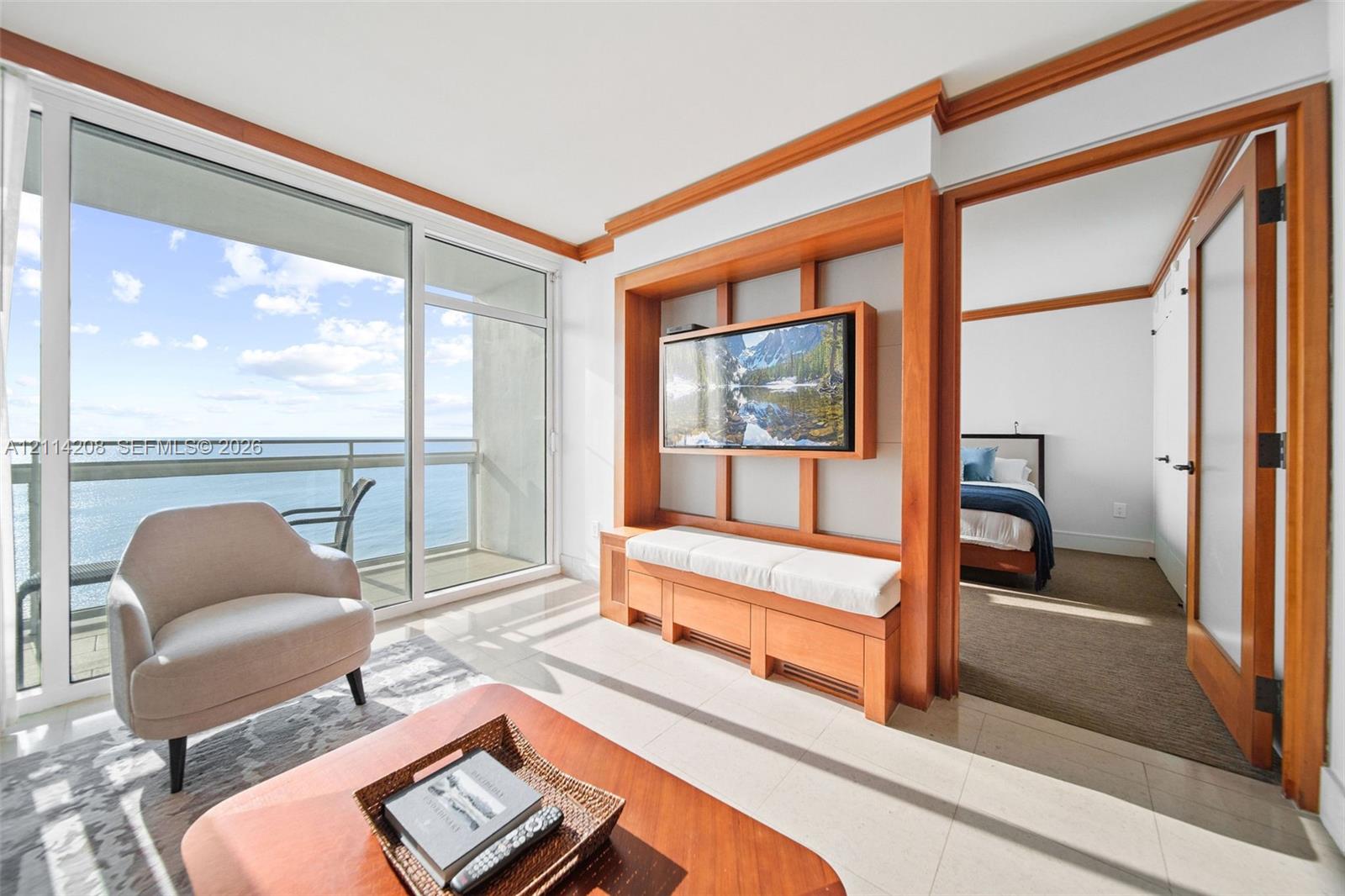 Floor-to-ceiling glass sliding doors opening to a balcony, custom built-in wood shelving with integrated media console, polished tile flooring, and interior wood-framed doors