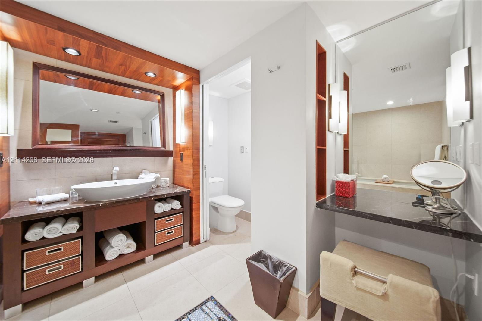 Custom wood-finish vanity with integrated storage, vessel sink, stone countertop, built-in shelving, and recessed lighting