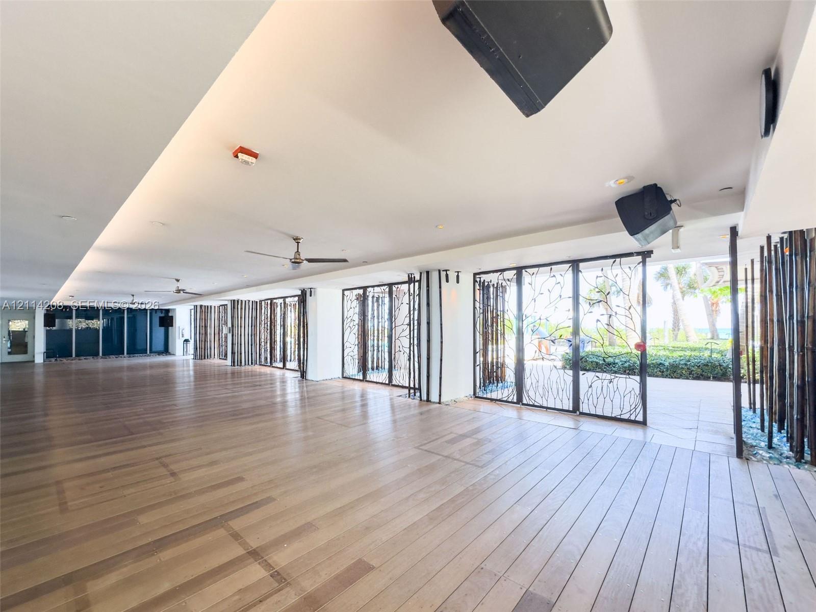 Expansive covered patio featuring wood-finish flooring, recessed ceiling lighting, ceiling fans, and decorative metal screens