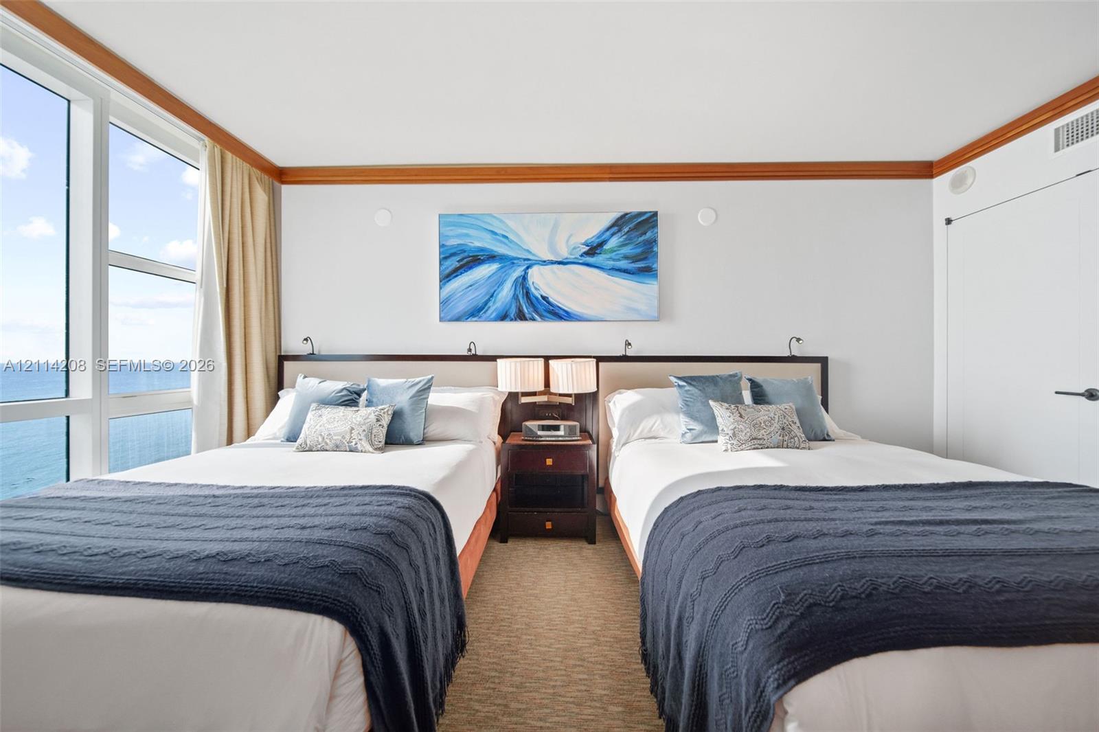 Floor-to-ceiling windows with ocean scenery, wood-trim crown molding, and neutral textured wall-to-wall carpeting