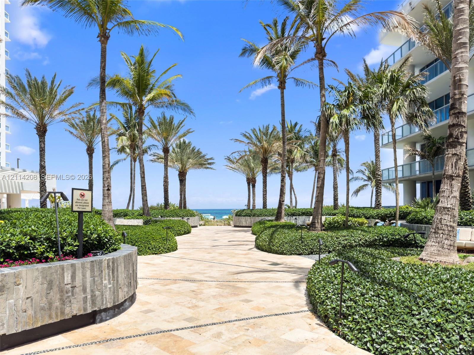 Landscaped courtyard featuring stone-paved walkways, mature palm trees, stacked stone planters, and manicured shrubbery