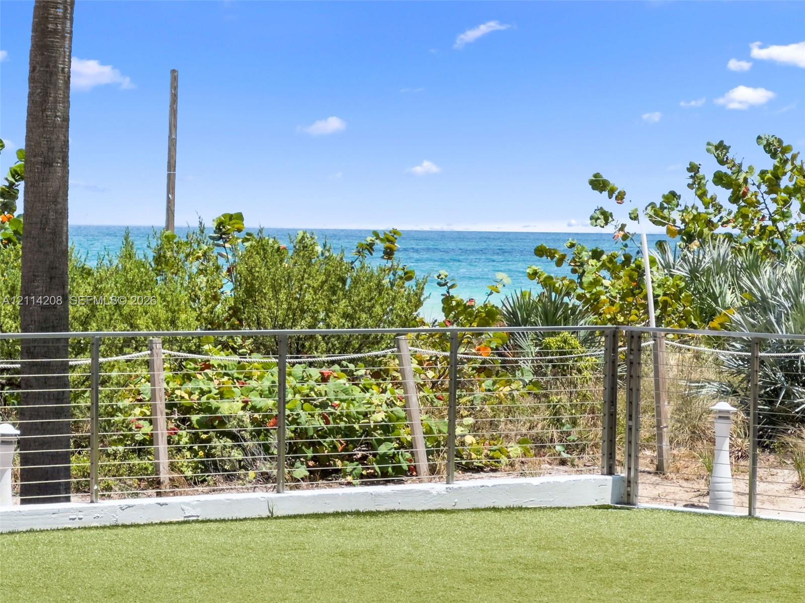 Artificial turf lawn enclosed by a stainless steel cable railing system, overlooking mature coastal landscaping and the ocean