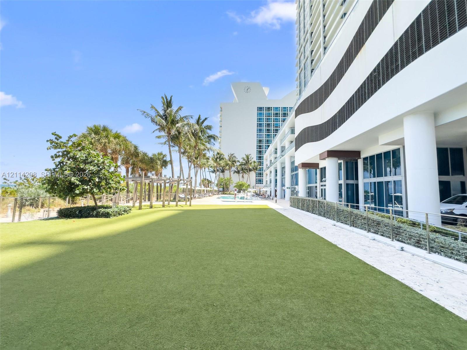 Expansive artificial turf lawn featuring mature palm trees, a wooden pergola, and metal railings
