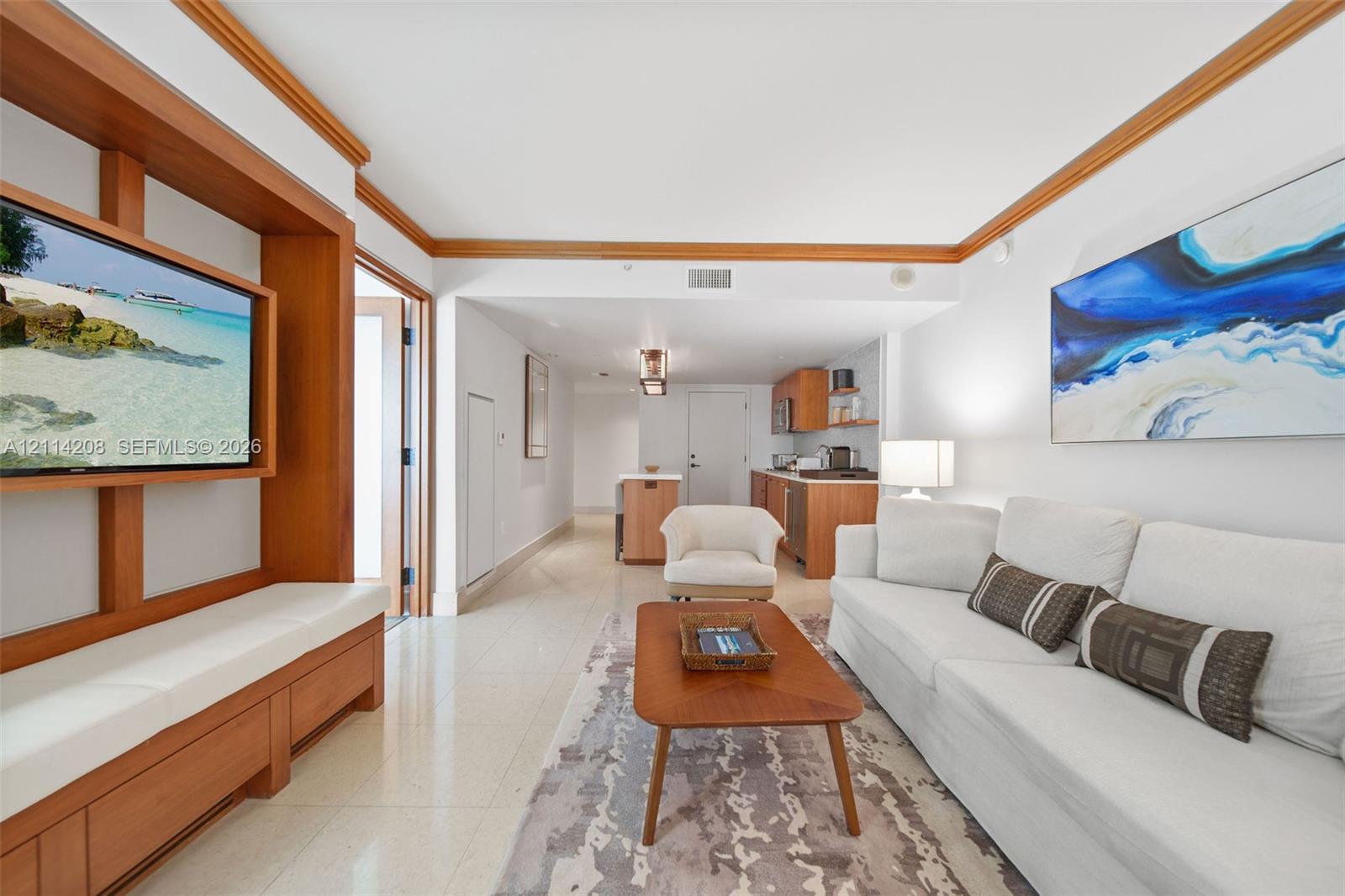 Custom built-in wood media console with integrated shelving, crown molding, tile flooring, and kitchen cabinetry