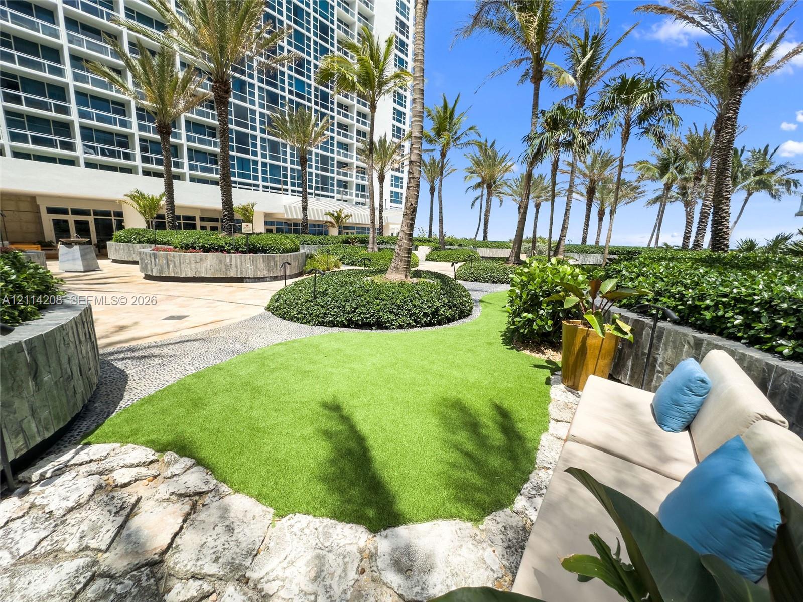 Landscaped terrace featuring palm trees, synthetic grass lawn, stone-tiled hardscaping, and circular concrete planters