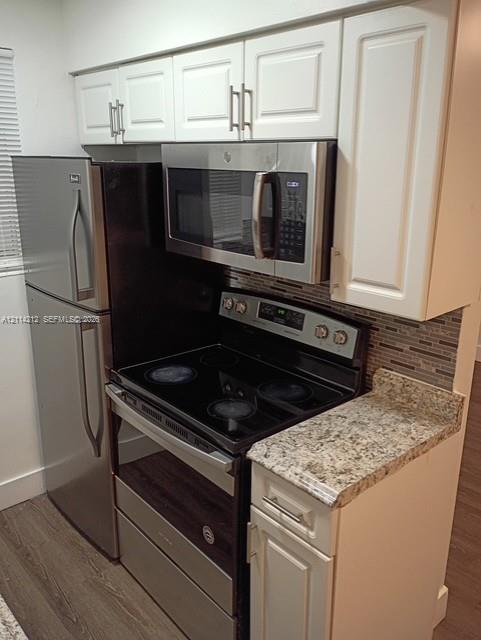 Kitchen area featuring white shaker-style cabinetry, stone-finish countertops, multi-tonal linear tile backsplash, and stainless steel appliances