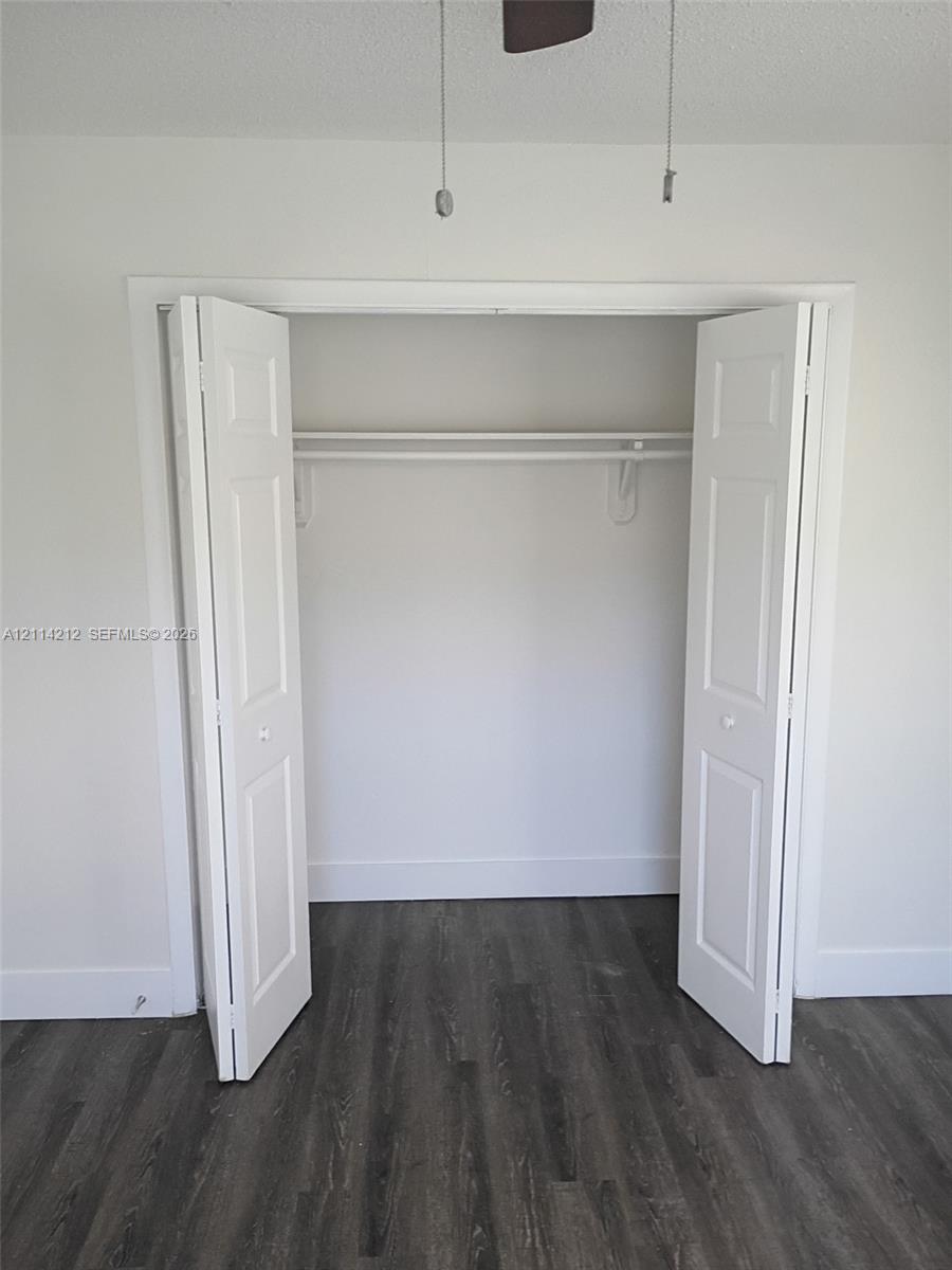 Storage closet featuring dual bifold doors and an integrated shelving rod, complemented by wood-finish flooring