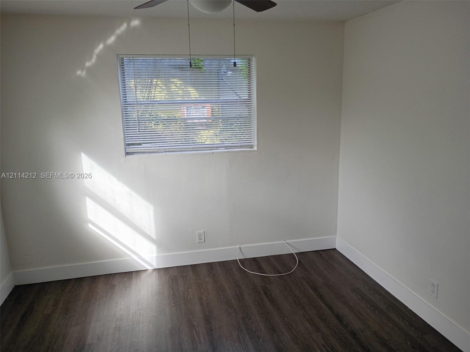 Neutral-toned interior space featuring wood-finish flooring and a ceiling-mounted light fixture with a fan