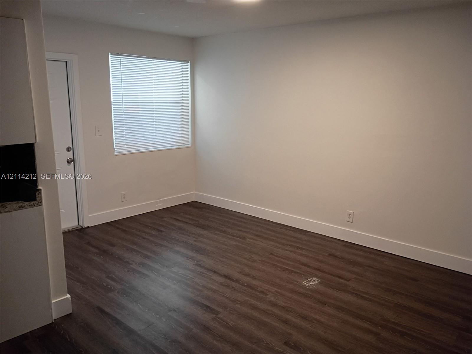 Room featuring wood-finish flooring, a single-panel white exterior door, and a horizontal window with white blinds
