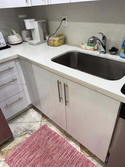 Glossy white cabinetry with modern metal pulls, light-toned composite countertops, undermount stainless steel sink, and polished chrome faucet