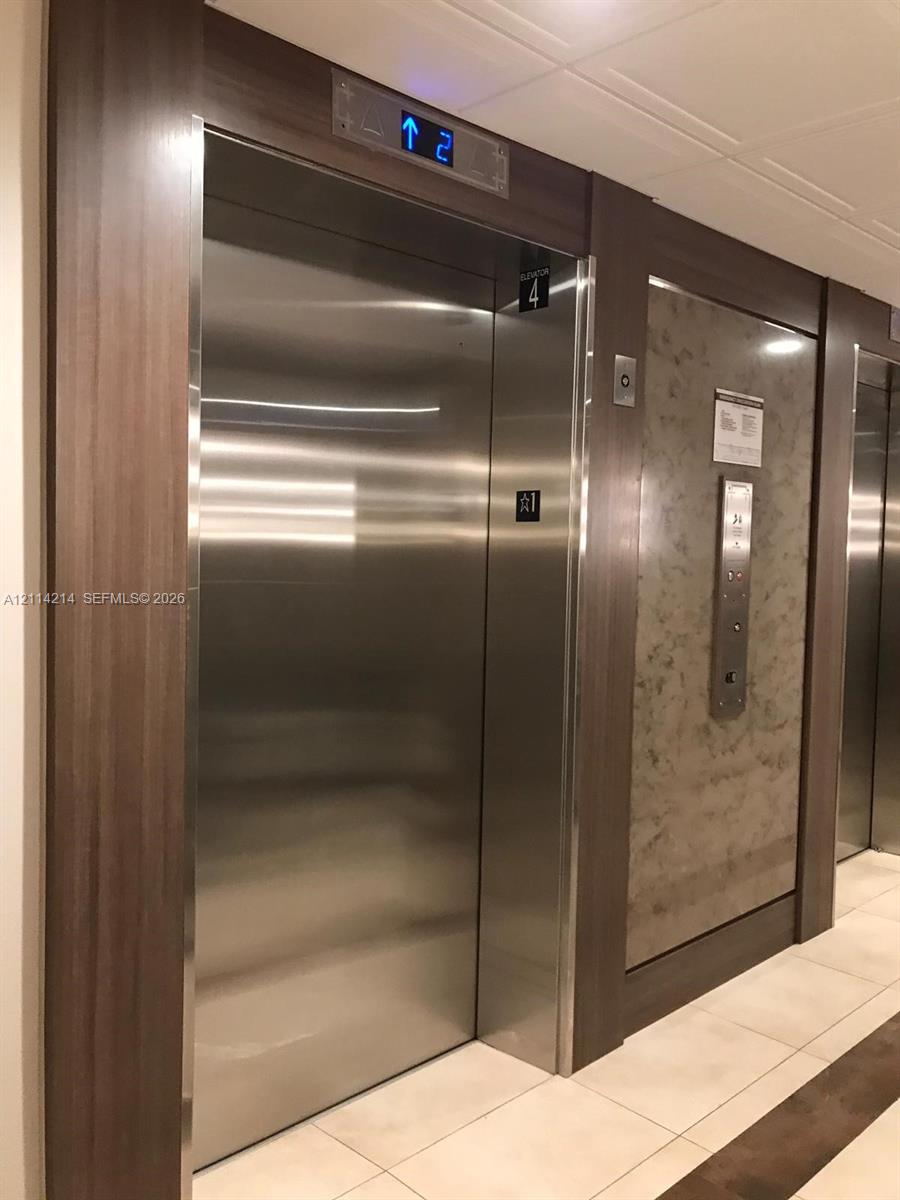 Elevator access featuring brushed stainless steel doors, floor-level digital display, wood-finish trim, and decorative stone-patterned paneling