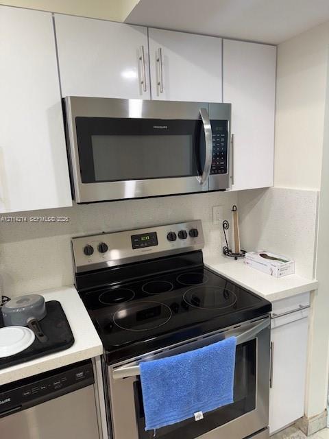 Kitchen featuring white slab-front cabinetry, stainless steel over-the-range microwave, stainless steel electric range with smooth cooktop, and stone-finish countertops