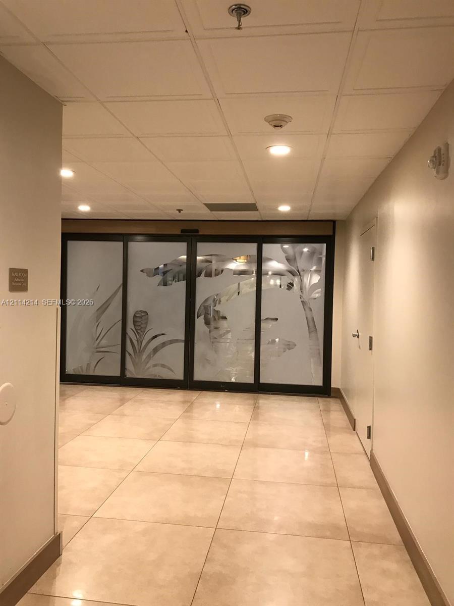 Neutral-toned tile flooring, recessed ceiling lighting, and floor-to-ceiling glass panel doors featuring frosted botanical-patterned detailing